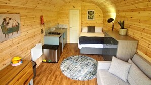 A cozy, wooden cabin interior with a bed, sofa, kitchen area, and a dining table.