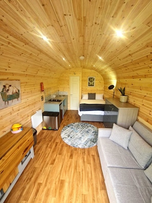 L’intérieur d’un chalet en bois chaleureux et accueillant, avec un lit, un canapé, un coin cuisine et une table à manger.