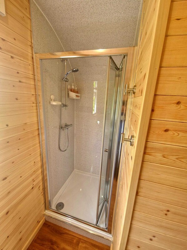 A wooden-paneled room with a glass-enclosed shower area, a wooden door, and a small shelf with toiletries. - The Star Inn (Llanbrynmair)