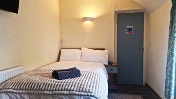 A hotel room with a bed, bedside table, lamp, and a door with a sign.