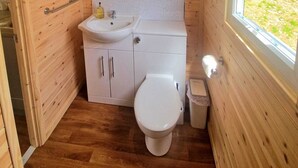 A compact wooden bathroom with a sink, toilet, and a window.