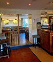 A bar area with stools, a counter, and a view into a dining area with tables and chairs.