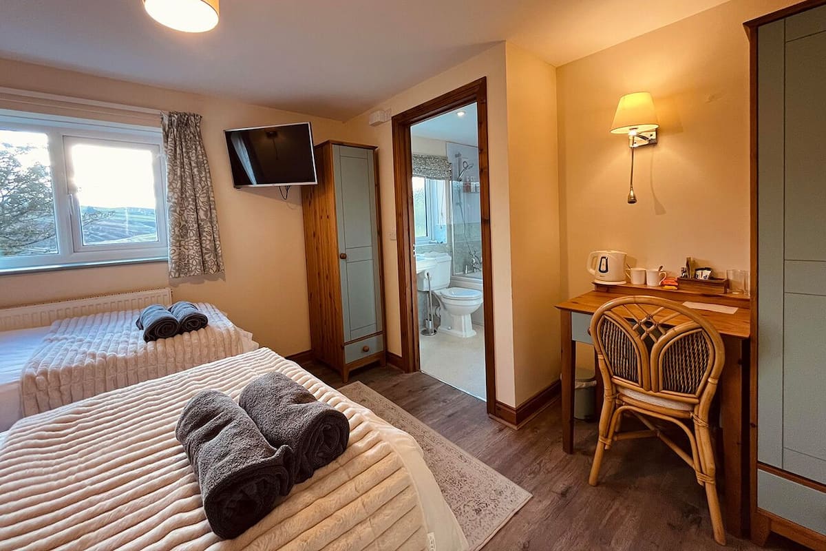 Camera d'albergo con due letti, una scrivania, una sedia, una televisione e un bagno visibile attraverso una porta aperta.