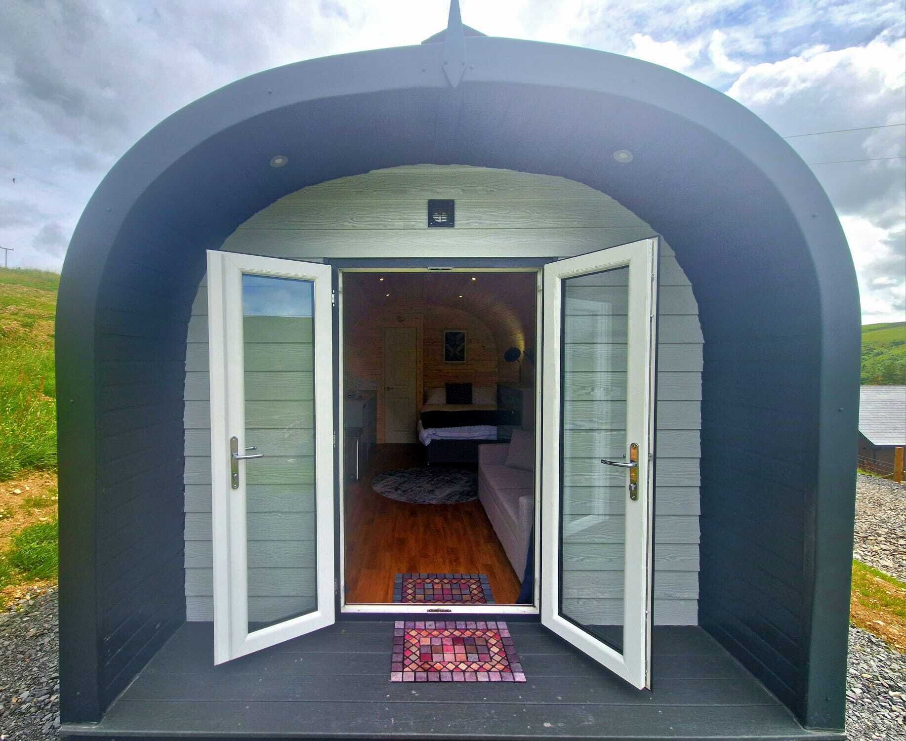 A small, enclosed structure with a single bed and a door, featuring a clear view into the interior.