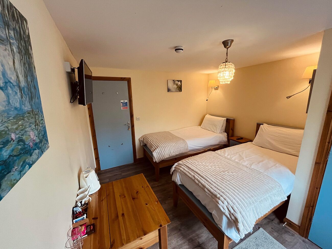 Una habitación pequeña y acogedora con dos camas individuales, una mesa de madera, un televisor y un cuadro en la pared.