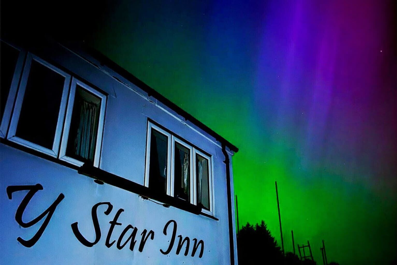 A building with the sign 'Y Star Inn' under a night sky with green aurora.