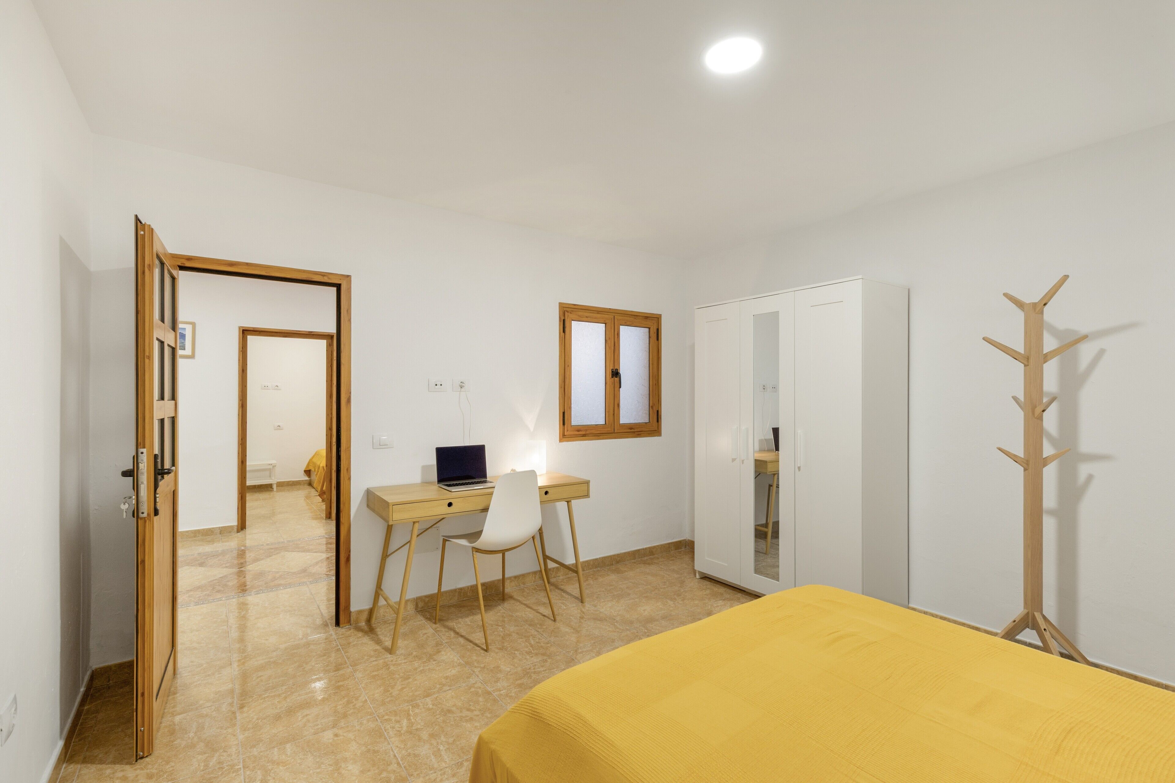 Ein Schlafzimmer mit einem Bett, einem Schreibtisch mit Stuhl, einem Kleiderschrank und einem Kleiderständer.