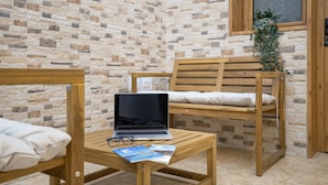 A room with a stone wall, a wooden bed, a wooden chair, a wooden table with a laptop and glasses, and a plant.