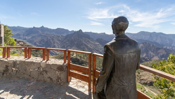 A statue of a man overlooking a mountainous landscape.
