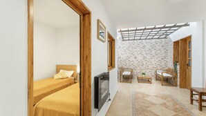 A room with a bed, a TV, a wooden door, a small table, and a seating area with a bench and a chair.
