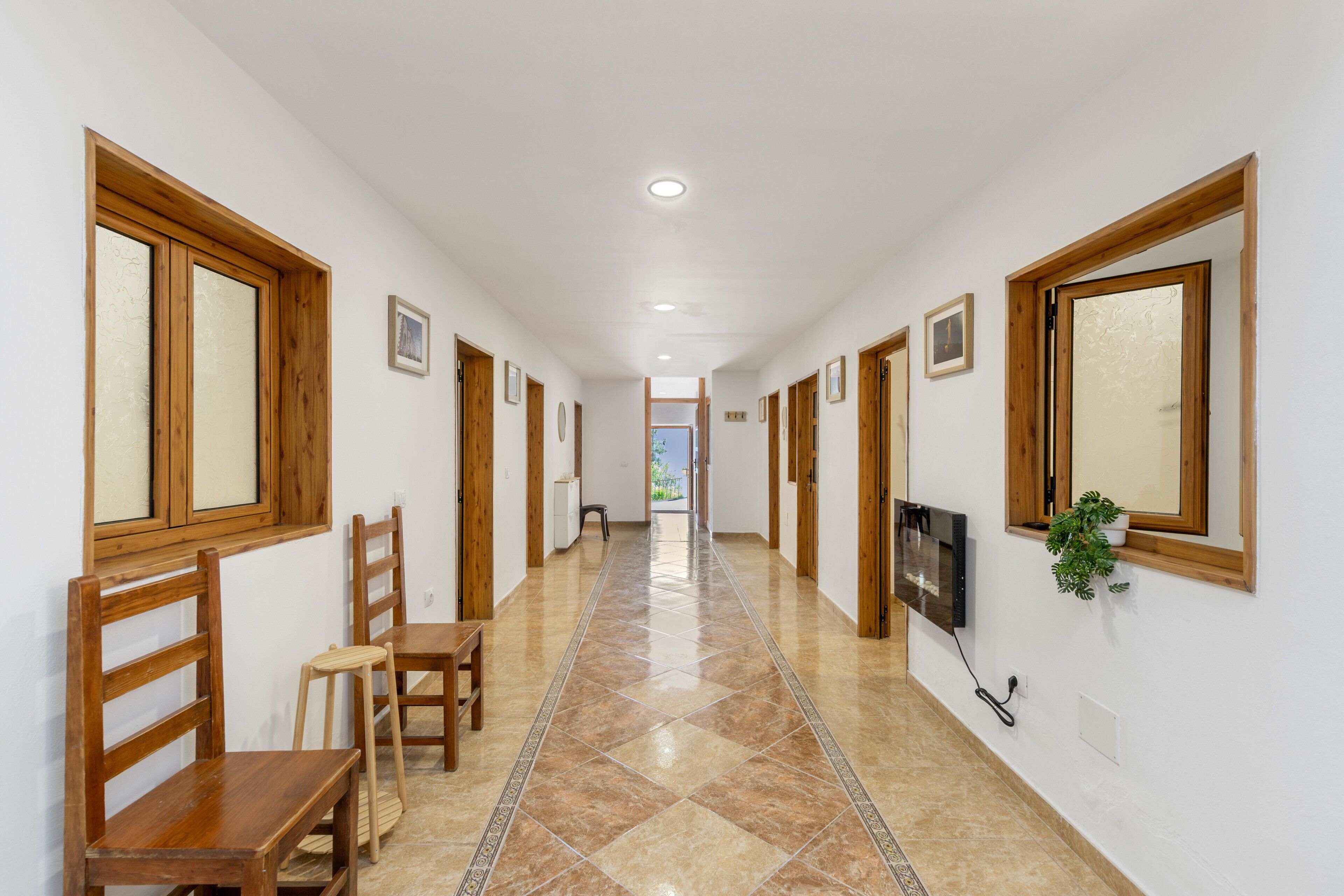 Un passadís amb portes de fusta, un televisor penjat a la paret i un paviment de rajoles.