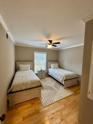 Ein Schlafzimmer mit zwei Betten, einem Deckenventilator, einem Fenster und Holzboden.