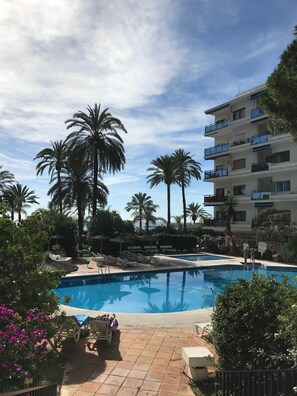 Ein Poolbereich mit Liegestühlen, Palmen und einem Gebäude mit Balkonen.