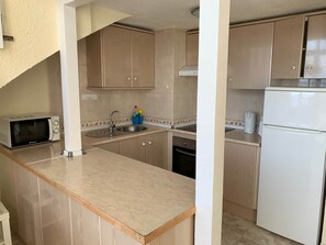 Eine Küche mit Holzschränken, einer Mikrowelle, einem Spülbecken und einem Kühlschrank.