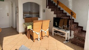 Ein Wohnzimmer mit Fernseher, Korbstühlen, einer Treppe und einem Küchenbereich.