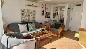 Ein Wohnzimmer mit einer Couch, Sesseln, einem Couchtisch und einer Wand-Klimaanlage.