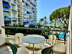 A balcony with a table and chairs, overlooking a pool and a building with multiple balconies. - 2. Skol Marbella 337B (Marbella)