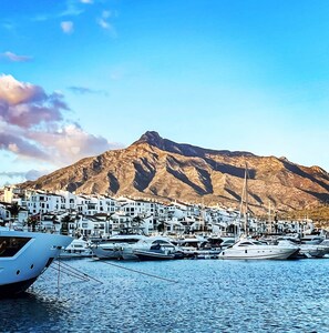 Ein Yachthafen mit vertäuten Booten, ein Berg im Hintergrund und weiße Gebäude mit Balkonen.