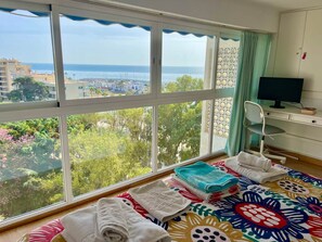 Ein Zimmer mit großem Fenster, einem Schreibtisch mit Computer und einem Bett mit Handtüchern.