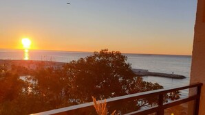 Een tafel met een vaas, kopjes en een bord eten op een balkon met uitzicht op een zonsondergang boven de zee.