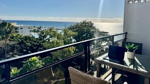 Un balcón con vistas a la playa, una computadora portátil y una planta en maceta.
