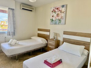 Hotellihuone, jossa on kaksi sänkyä, yöpöytä, taulu ja ikkuna, jossa on verhot.