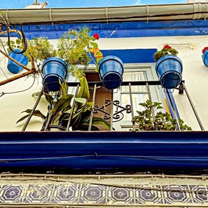 Ein Gebäude mit einer blau-weißen Fassade, Metallfenstergittern und drei blauen Blumentöpfen am Balkon.