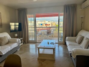 A hotel room with a balcony, a flat-screen TV, a table with a glass, and two sofas. - 3. Parque Marbella 27B (Marbella)