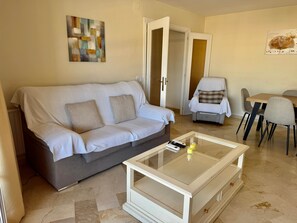 A living room with a sofa, a glass coffee table, a dining table with chairs, and artwork on the walls. - 3. Parque Marbella 27B (Marbella)