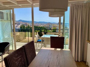 Ein Balkon mit Tisch und Stühlen, Blick auf eine Stadtlandschaft und ein großes Fenster.
