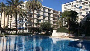 Ein Hotel mit Swimmingpool, Palmen und einem mehrstöckigen Gebäude mit Balkonen.