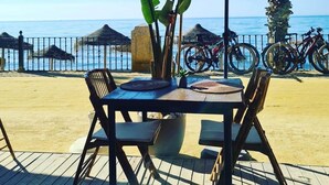 Un tavolo con sedie e un grande ombrellone, con vista su una spiaggia con biciclette e una recinzione.