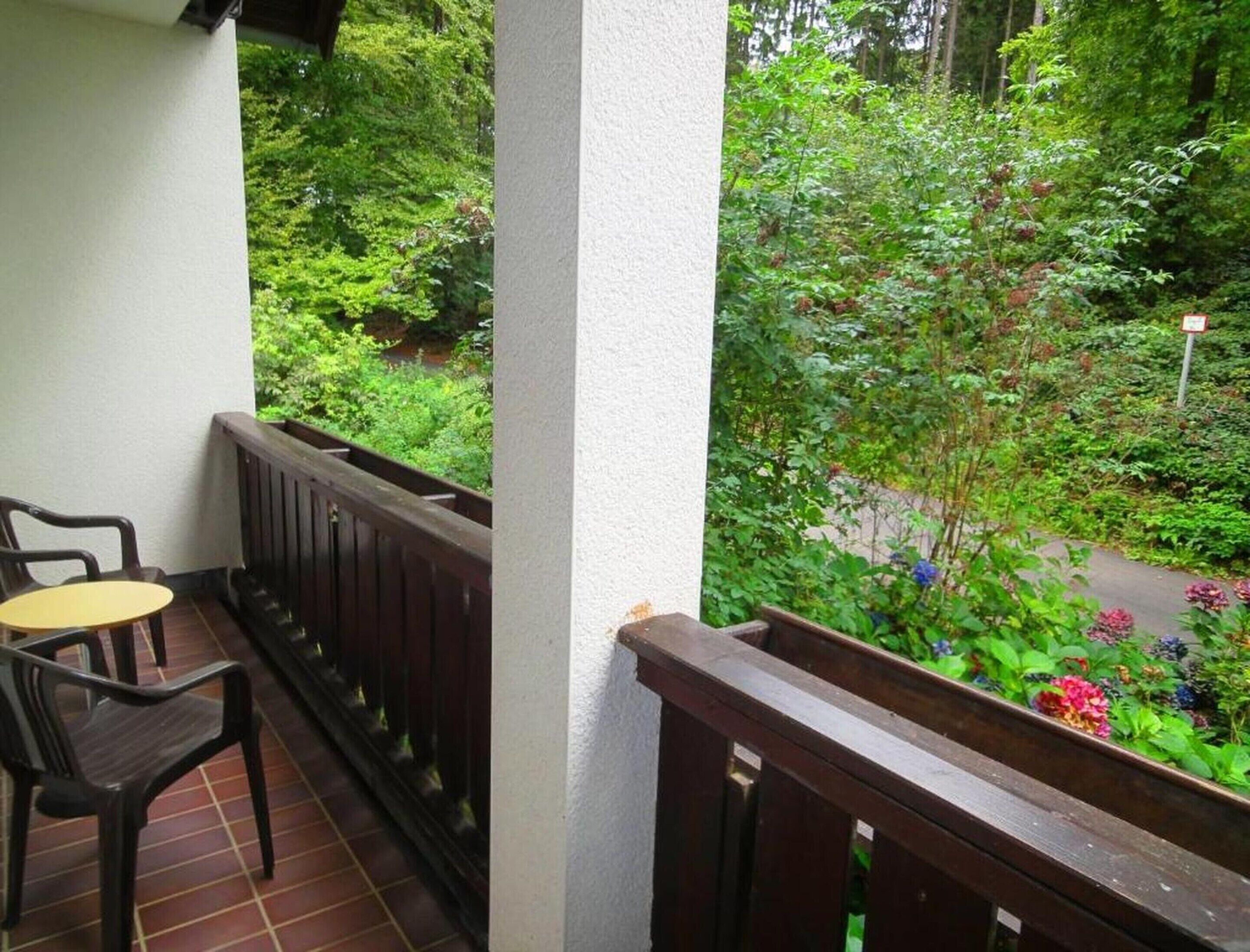 Un balcón con vistas a un jardín exuberante, baranda de madera y una pequeña mesa con sillas.
