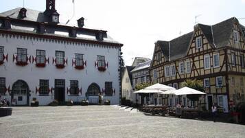 A cobblestone square with historic buildings, a clock tower, and outdoor seating areas.