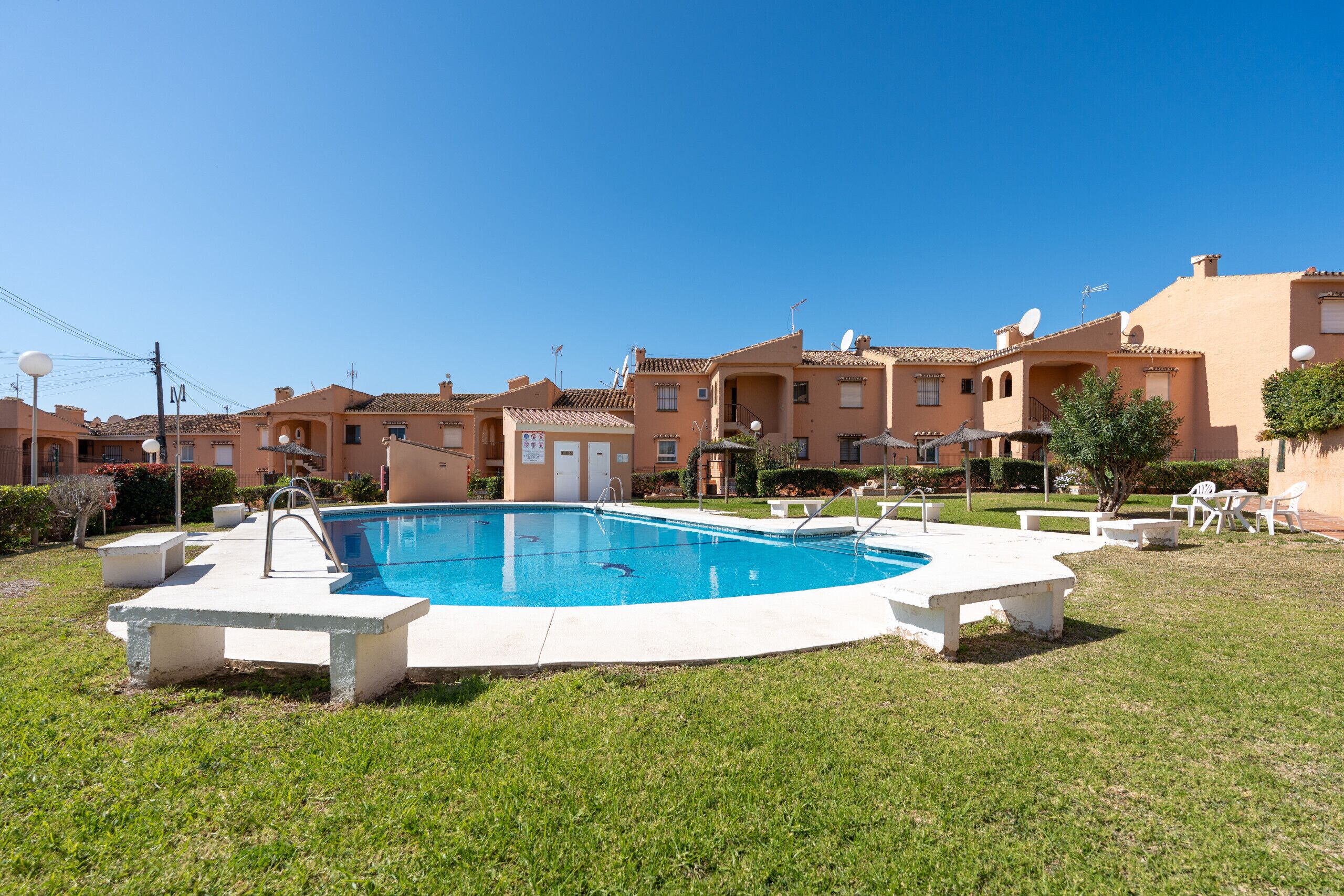 A swimming pool surrounded by a grassy area with a row of residential buildings in the background.