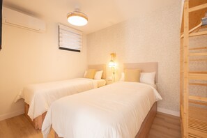 Ein Zimmer mit zwei Betten, darunter ein Holzbettkasten, einem Deckenventilator, einer Wandklimaanlage und einem Fenster mit Jalousien.