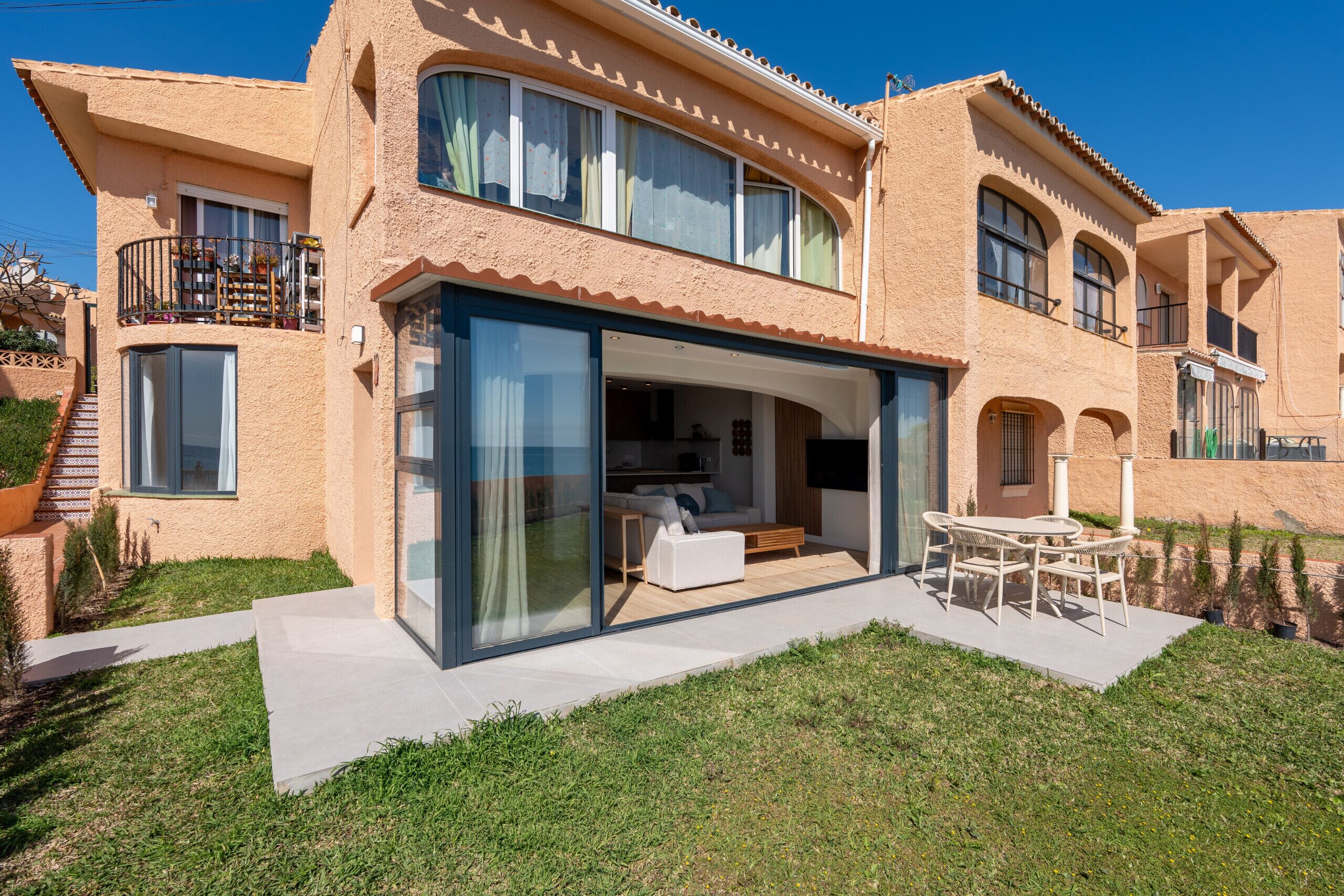 Una casa a due piani con veranda in vetro, posti a sedere all'aperto e una scala che conduce al piano superiore.