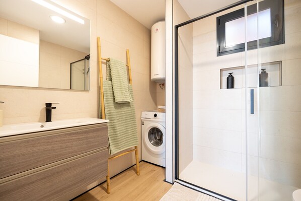 Ein modernes Badezimmer mit einem Holzkosmetikschrank, einer Waschmaschine und einer Duschkabine aus Glas.