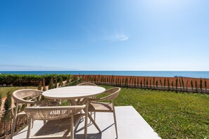 Eine Terrasse mit Tisch und Stühlen, Blick auf das Meer und eine Reihe von Bäumen.