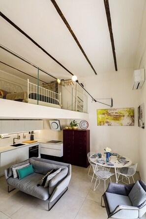Um apartamento moderno com quarto no mezanino, cozinha compacta, área de jantar e espaço para sentar.