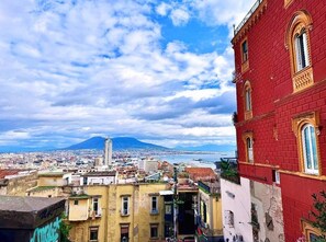 A cityscape with a prominent red building, a distant mountain, and a body of water. - Calm and quiet apartment in the heart of Naples (Napoli)