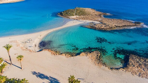 Ein Küstenstrand mit klarem türkisblauem Wasser, Sandstrand und Felsformationen.