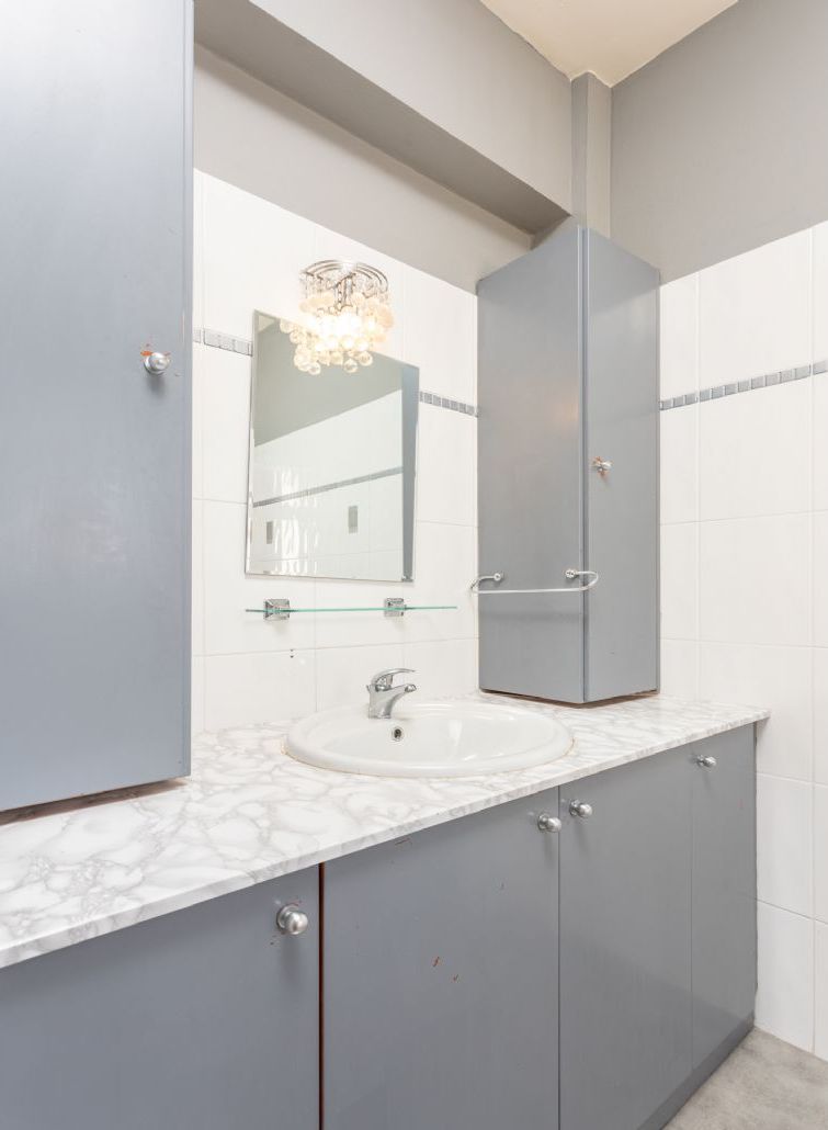 A bathroom with a marble sink, a large mirror, and grey cabinets.