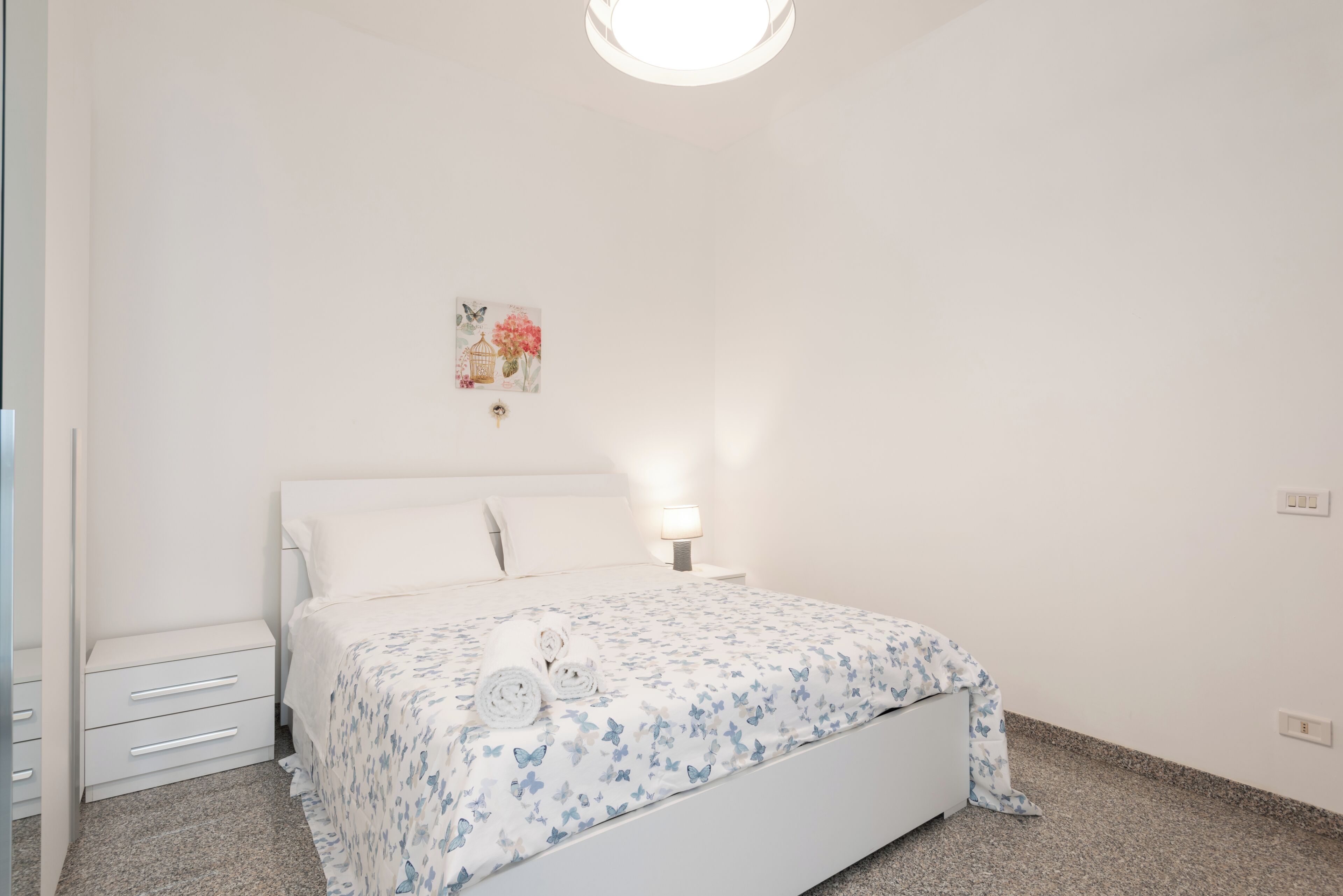 Ein Schlafzimmer mit einem Bett, einem Nachttisch, einer Wandleuchte und einem kleinen Gemälde.