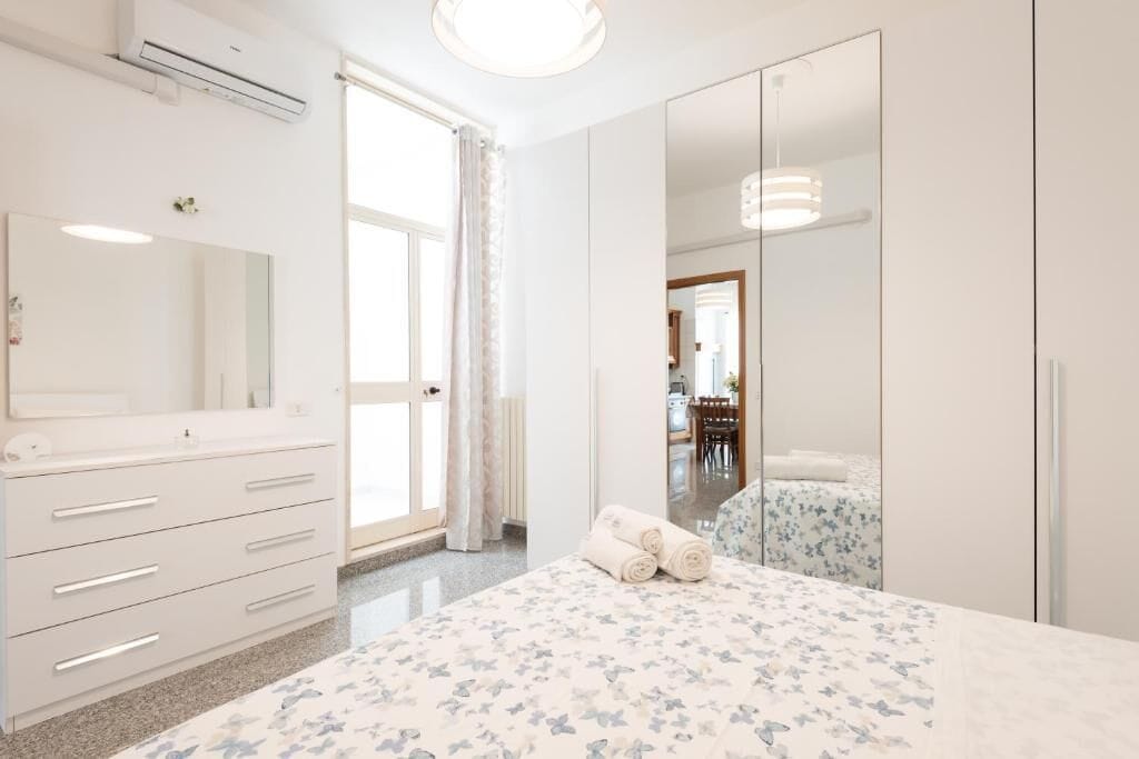 A bedroom with a bed, a dresser, a mirror, a wardrobe, and a window with curtains.