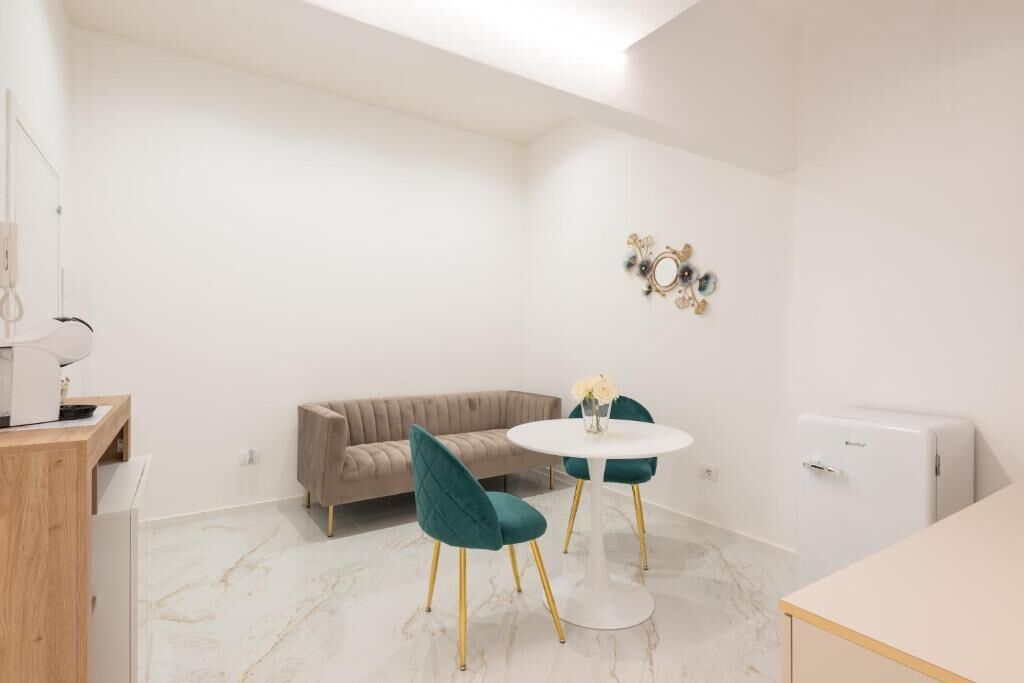 Una habitación moderna con sofá, dos sillones, una mesita pequeña, refrigerador y un elemento decorativo en la pared.