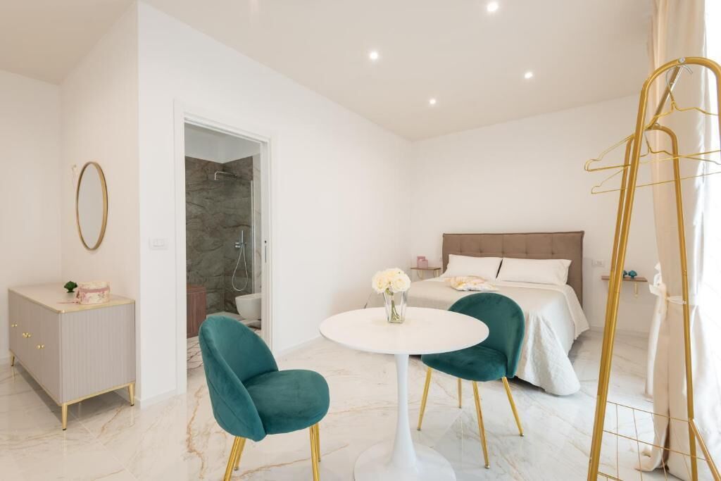 A modern hotel room with a bed, two chairs, a small table, a wardrobe, and a shower area.
