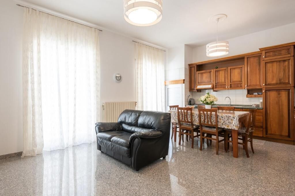 A living room with a black leather sofa, a dining table with chairs, wooden cabinets, and a kitchen area with wooden cabinets and a countertop.
