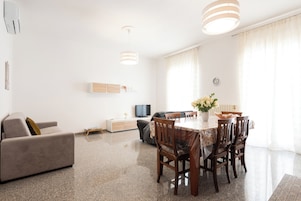 En moderne stue med sofa, spisebord, stole og fjernsyn.