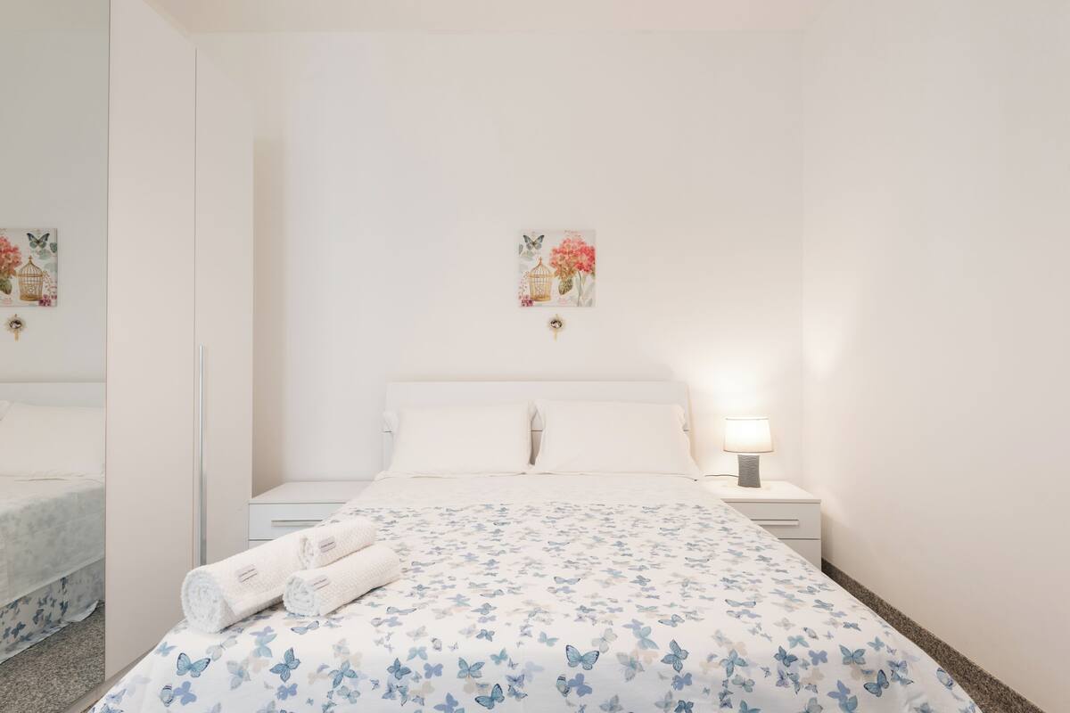 Un dormitorio con cama, mesitas de noche, lámpara y obras de arte en la pared.